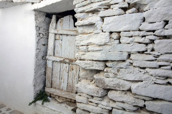 stock image Aged weathered white stonewall background, door covered with broken peeled plank. Old stone wall structure, Cyclades island, Greece.