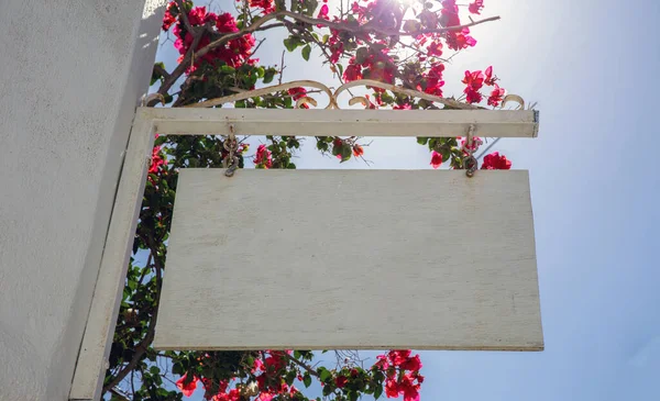 金属構造からぶら下がっ空の白い木製の看板 ブーゲンビリアピンクの太陽の空の背景キクラデス島ギリシャ コピースペース広告テンプレートの表示 — ストック写真
