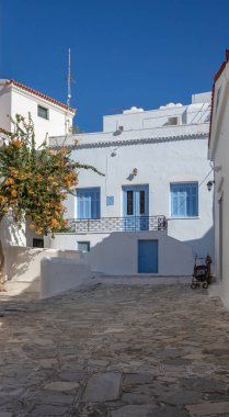 Yunanistan, Tinos Adası, Hora kasabası. Kiklad mimari evi cephesi beyaz ve mavi renkli, asfalt kaplı dar bir sokak, yaz güneşli bir gün. Dikey
