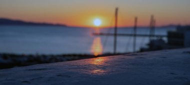 Günbatımı Tinos Adası, Cyclades, Yunanistan 'da. Bulanık renkli gökyüzü ve Ege mavi denizi, bulanık gemi direği silueti, parlak altın güneş arka planı.