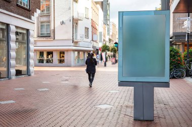 İlan panosu boş mavi panel, şehir merkezinde güneşli bir günde dükkânı olan bir kadın yaya yolunda yürüyor. Ad şablonu, boşluğu kopyala