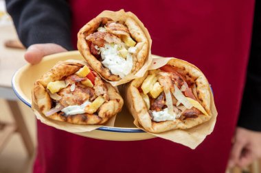 Kırmızı önlüklü garson üç adet Gyro Pita Shawarma, Souvlaki tabağı sunar. Fast food, Yunan ve Türk et paketleri, kapayın..