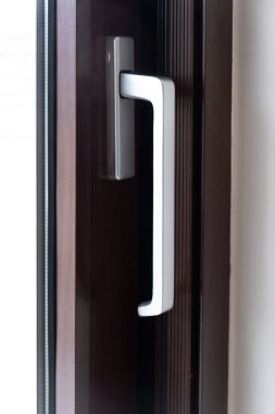 Kapıda alüminyum gümüş kapı kolu, kahverengi çerçeve arka planında pencere. Modern stil güvenli yapıya yakından bakın. Dikey