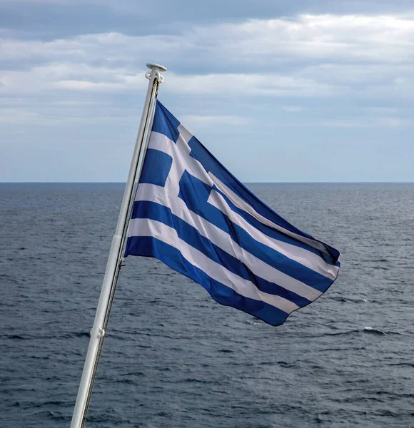 stock image Greece sign symbol of leading shipping power in the world. Greek flag on flagpole waving over rippled sea water. Cloudy sky background.