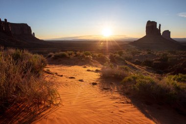 Anıt Vadisi siluetinin üzerinde gün batımı, güneş ışığı boş çölün kumunu ve gökyüzünü renklendiriyor. Navajo Kabile Parkı, ABD, Utah, Arizona. Boşluğu kopyala