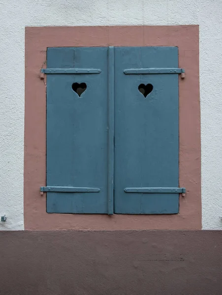 白色石墙背景上有蓝色关闭木百叶窗的窗户 有心孔的百叶窗 爱的象征 — 图库照片