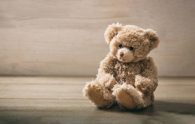 Oyuncak ayı boş bir tahta zeminde oturuyor. Tahta masadaki kahverengi, üzgün, tüylü hayvan oyuncağı. Doğum günü, sevgililer günü, Noel hediyesi. Boşluğu kopyala