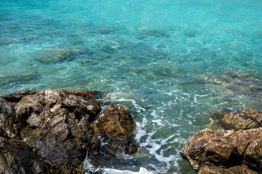 Foamy wave breaks on rock in clear, transparent, turquoise sea water background. Greece Agistri island Aponisos beach. Above view clipart