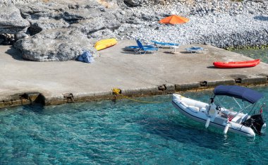 Şişme tekne limanda demirlemiş durumda. Kayalık manzaranın önündeki şempanze ve şezlong. Yaz güneşli bir gün, dinlenme, dinlenme..