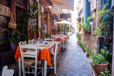 Girit adası Yunanistan 'daki Chania Old Town' da geleneksel meyhane. Boş sandalye masası, saksı çiçeği, asfalt sokak, yaz günü..