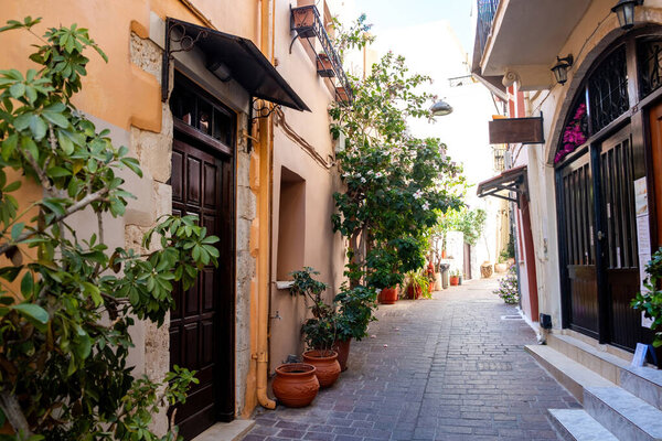 Crete island Greece, Chania Old Town. Multicolor traditional building and shop, pot with plant on narrow empty paved alley, summer sunny day.