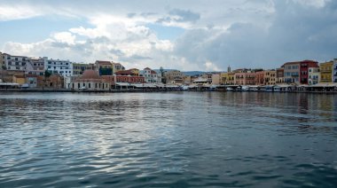 Chania Town Girit, Yunanistan. Açık havanın panoramik manzarası, deniz kenarındaki geleneksel bina ve kilise. Dalgalanan karanlık deniz, bulutlu gökyüzü arkaplanı.