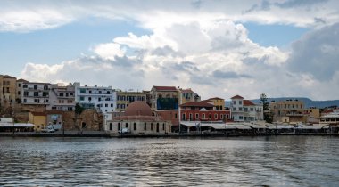 Chania Town Girit, Yunanistan. Açık havanın panoramik manzarası, deniz kenarındaki geleneksel bina ve kilise. Dalgalanan karanlık deniz, bulutlu gökyüzü arkaplanı.