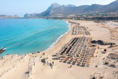 Falasarna kumlu plajı, Girit adası Yunanistan. Şemsiye, deniz kenarı güneş yatağı dalgalı deniz suyu, yazın ünlü tatil manzarası..