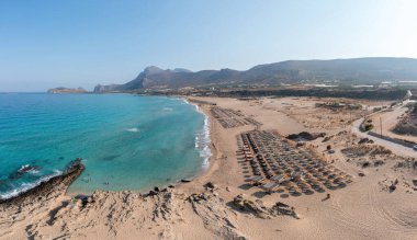Phalasarna kumlu plajı, Girit adası Yunanistan. Şemsiye, deniz kenarı güneş yatağı dalgalı deniz suyu, yazın ünlü tatil manzarası..