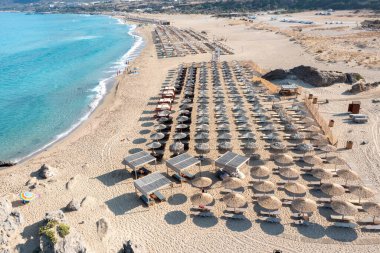 Falassarna kumlu plajı, Girit adası Yunanistan. Şemsiye, deniz kenarı güneş yatağı dalgalı deniz suyu, yazın ünlü tatil manzarası..