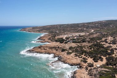 Girit, Yunanistan, Gavdos adası. Dalgalanan deniz suyunun hava aracı görüntüsü sahile sıçrıyor, vahşi manzara, mavi gökyüzü, doğa. Macera, yürüyüş, spor.