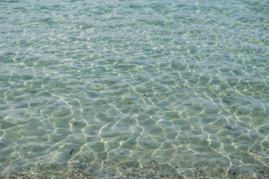 Açık, sığ, açık mavi deniz, şeffaf, ışıltılı su yüzeyi arka plan dokusu. Su altı çakıl taşı ve kum, Yunanistan 'a gidiyor. Boşluk