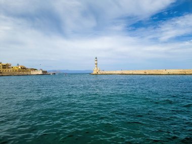 Chania 'nın eski kasabasındaki Venedik limanında deniz feneri. Dalgalı denizde dalgalı suyu olan taş fener kulesi, bulutlu gökyüzü, şehir binası. Girit Adası, Yunanistan.