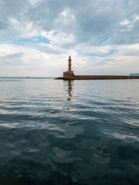 Beacon at Venetian harbour in Old Town of Chania. Reflection of lighthouse tower in wavy sea, stone breakwater. Crete island, Greece. Vertical clipart