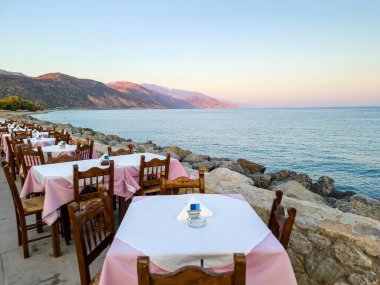 Paleochora köyündeki geleneksel sahil tavernası, Girit Adası Yunanistan 'da öğleden sonra. Taverna restoranı, boş sandalye masası, asfalt sokak..