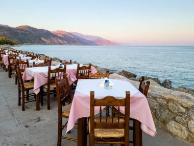Paleochora köyündeki geleneksel sahil tavernası, Girit Adası Yunanistan 'da öğleden sonra. Taverna restoranı, boş sandalye masası, asfalt sokak..