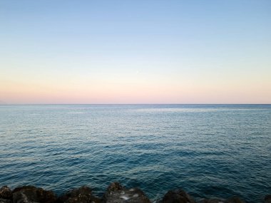 Mor, pembe, mavi gökyüzü arkaplan dokusuna karşı dalgalanan boş deniz. Dalgalı mavi okyanus suyu yüzeyi. Öğleden sonra Rocky Sahili 'nde, kopyalama alanı.