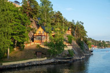 Old traditional villa at seaside of Sandhamn, Archipelago, Stockholm Sweden. Reflection of cottage in sea water, view of nature from cruise boat. clipart