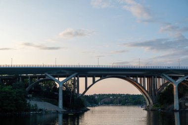 Skurubron, Skuru Arched Bridge, Nacka Belediyesi, Archipelago Stockholm İsveç. Çok renkli gökyüzü ve deniz suyu, yolcu teknesinden manzara. 