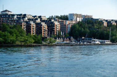 Stockholm County, Archipelago İsveç 'te Nacka Strand marinası. Deniz kıyısında bir bina, iskeleye demirli bir yat, sakin deniz suyu, yaz günü..