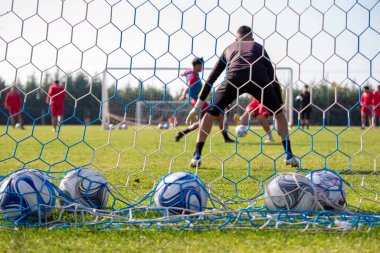 Futbol sahada. Ağ ve takım antrenmanlarının arkasında yeşil çimlerde futbol topu var. Spor, rekabet, eğlence..
