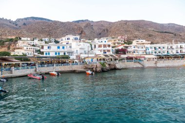 Girit Adası, Yunanistan. Rethymno şehri ve limanındaki açık deniz manzaralı kafe tavernası. Demir atmış tekne, dalgalı deniz suyu, mavi gökyüzü arka planı.