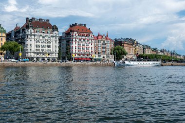 Rıhtım limanına demirlemiş gezi teknesi. Deniz kıyısındaki heybetli renkli bina, Stockholm, İsveç kültürü.