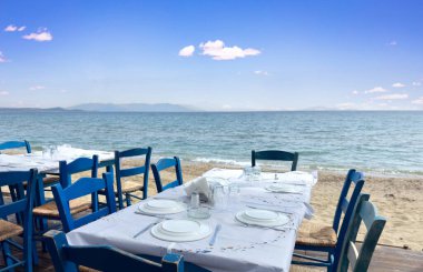Yunanistan 'da açık hava geleneksel deniz tavernası. Taverna restoranı, boş ahşap mavi sandalye tabaklar, kumlu plaj, deniz, yaz günü.