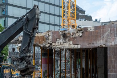 Bina yıkım konsepti. İnşaat alanındaki yıkılmış binanın önündeki kazıcı, eski inşaat harabelerine karşı yeni bir yapı arka planı.