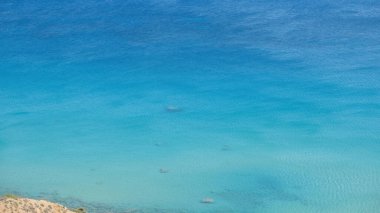 Dalgalı deniz suyu, kumlu zeminin üstünde, arka planda birkaç çakıl taşı, kopyalama alanı. Yunan deniz manzarası, doğa. Yaz tatili şablonu