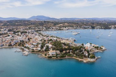Yunanistan, Mora 'nın Argolis kentindeki bir yaz tatil beldesi olan Porto Cheli' nin insansız hava aracı görüntüsü. Kıyıdaki deniz kenarındaki binalar ve denizdeki tekneler, mavi gökyüzü.