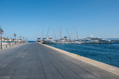 Spetses Adası, Yunanistan. Yatlar ve yelkenliler marinada demirli, mavi gökyüzü. Boş asfalt gezinti güvertesi