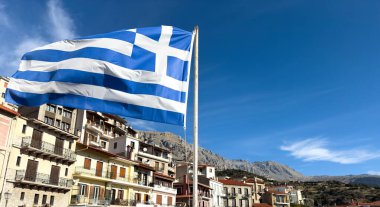 Yunanistan. Yunan bayrağı dalgalanması, Arachova köyü binaları ve mavi gökyüzü arka planı. Kış sporları için turizm merkezi, Parnassos Dağı, Viotia.