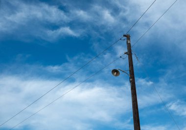 Retro sokak lambası, ahşap elektrik direğinde klasik ampul. Eski moda sütun lambası, mavi bulutlu gökyüzü arkaplanı, kopyalama alanı