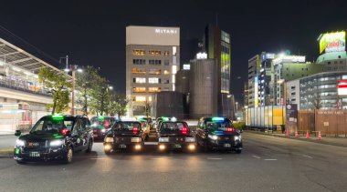 Japonya. Nagoya. Nisan 02, 2024. Taksi durağındaki siyah Japon taksisi. Park halindeki arabaların ışıkları açık, işyerindeki şoförler sağ tarafta oturuyor, geceleri binalar aydınlanıyor..