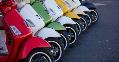 Sokakta yan yana park edilmiş yeni motorlu mobiletler. Arka arkaya renkli, renkli eski motosikletler.