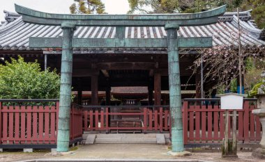 Japon tapınağı girişi geleneksel Torii kapısı, Japonya. Döşemeli çatı pavyonu ve kırmızı ahşap çit, çiçek açan ağaç. 