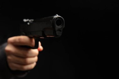 Silahlı ve yakın plan silahlı bir adam, karanlık arka planda tabanca tutan bir adam. Tehlike ve suç kavramı