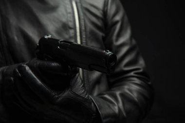 Silahlı bir adam, yakın plan bir silah tutuyor. Siyah arka planda deri eldivenli bir suçlu. Soygun ve suç kavramı