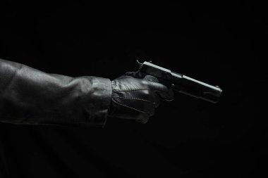 Karanlık arka planda bir silah, yakın görüş, deri eldivenli bir el tabanca tutuyor. Suç, cinayet kavramı