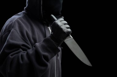 Eldivenli, siyah arka planda, silahlı saldırı konsepti olan kapüşonlu bir adam..