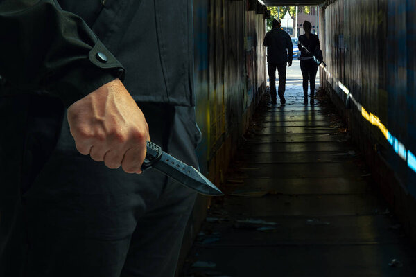 Преступник с ножом крупным планом, темный городской фон, концепция вооруженного нападения.