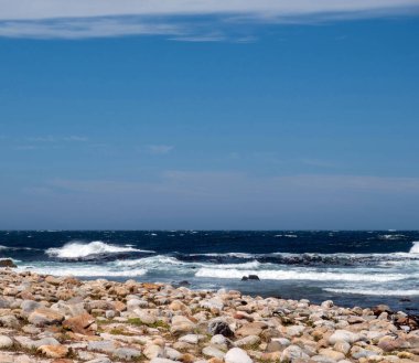 Okyanus dalgaları kayalık kıyılara çarpıyor, mavi gökyüzü dağınık bulutlarla