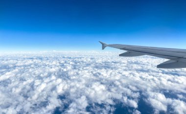 Bulutların üzerinde uçan uçak, uçak penceresinden görünen manzara, kabarık bulutlar ve mavi gökyüzü arka planı